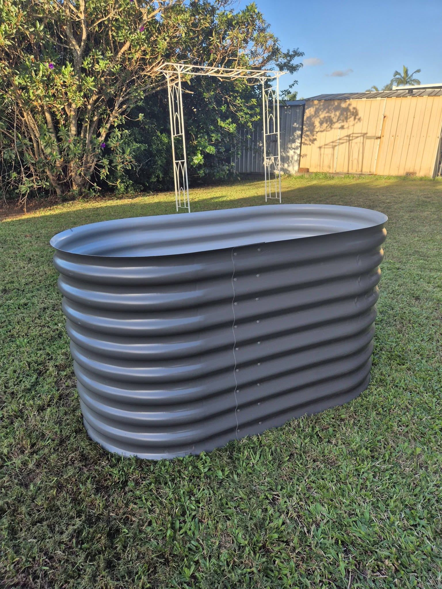 Corrugated aquaplate steel garden bed in woodland grey, photographed in a backyard at golden hour